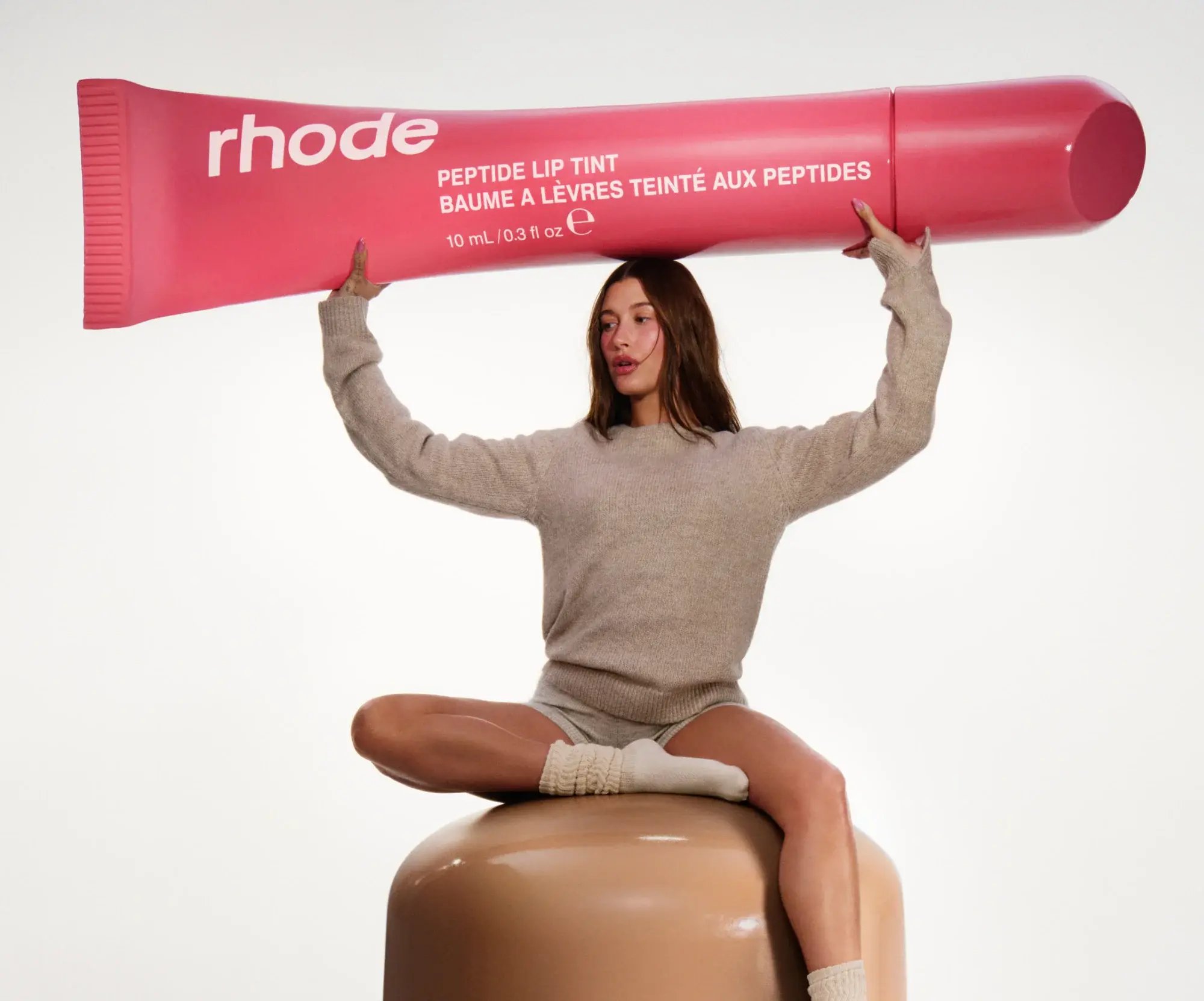 Oversized Product - the rhode peptide lip tint being held up above the model's head.