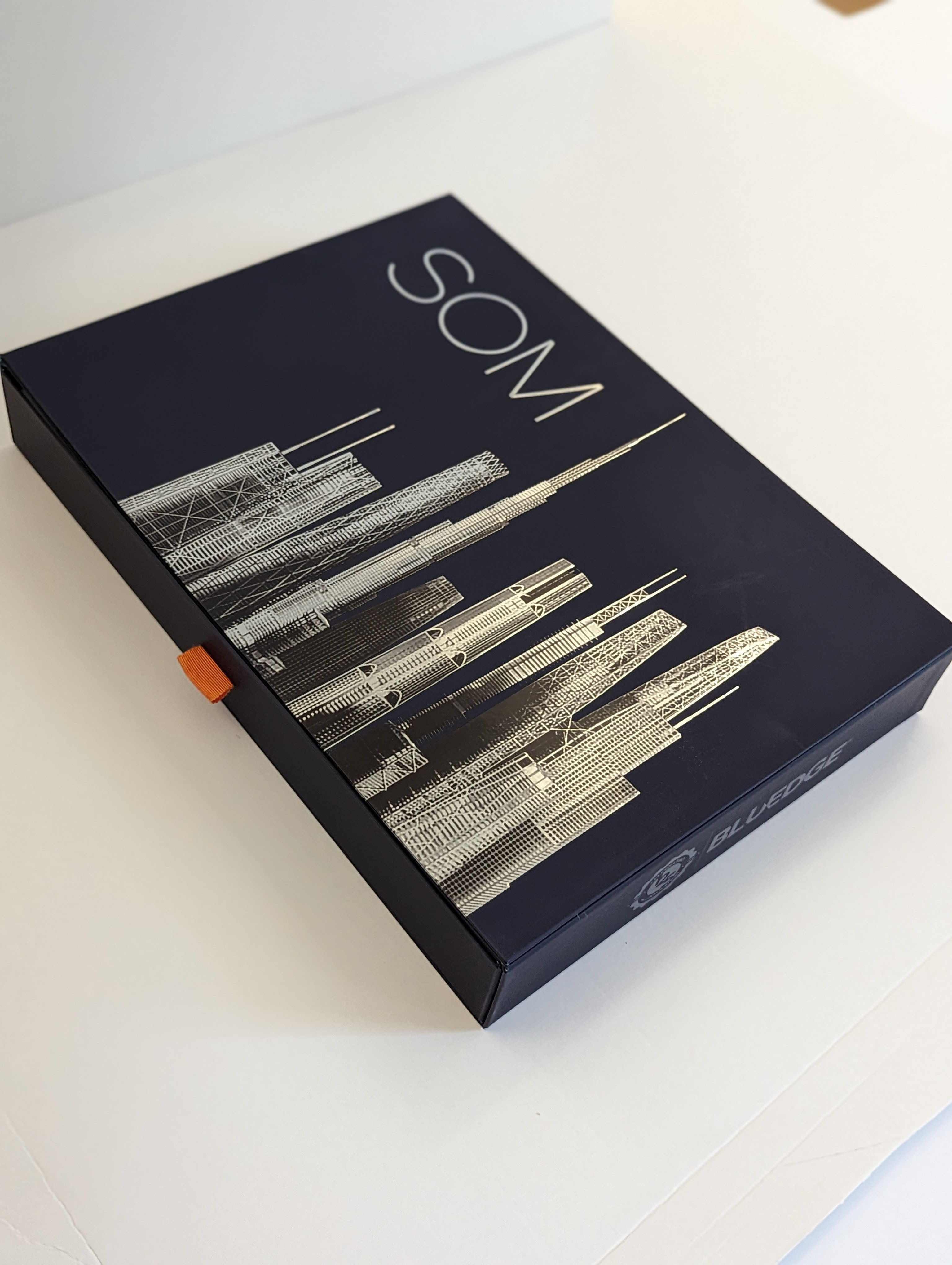 SOM Presentation Kit. Shown as a closed box with a sky line outline of Dubi in silver.